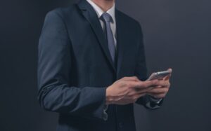 Businessman in black suit and necktie with holding smartphone on black background.